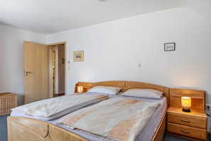 Una cama doble con cabecera de madera, dos mesitas de noche con lámparas, un armario de madera y una puerta que da a otra habitación.