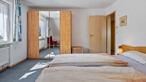 A hotel room with a bed, a wooden wardrobe, a mirror, a red chair, and a small wooden basket. - 'Gartenblick' Apartment with Mountain View, Private Terrace, and Wi-Fi (Schramberg)