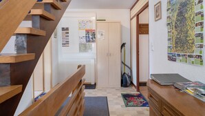 A staircase leading to a landing with a wooden handrail, a wall-mounted map, a desk with a vacuum cleaner, and a door with a calendar. - 'Gartenblick' Apartment with Mountain View, Private Terrace, and Wi-Fi (Schramberg)
