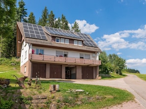 A two-story house with solar panels on the roof, a balcony with railings, and a garage. - 'Gartenblick' Apartment with Mountain View, Private Terrace, and Wi-Fi (Schramberg)