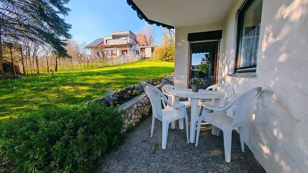 Een terras met een tafel en stoelen, een stenen muur en uitzicht op een huis met zonnepanelen.