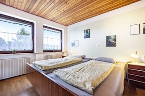 A room with two beds, wooden ceiling, large windows, and wall art.