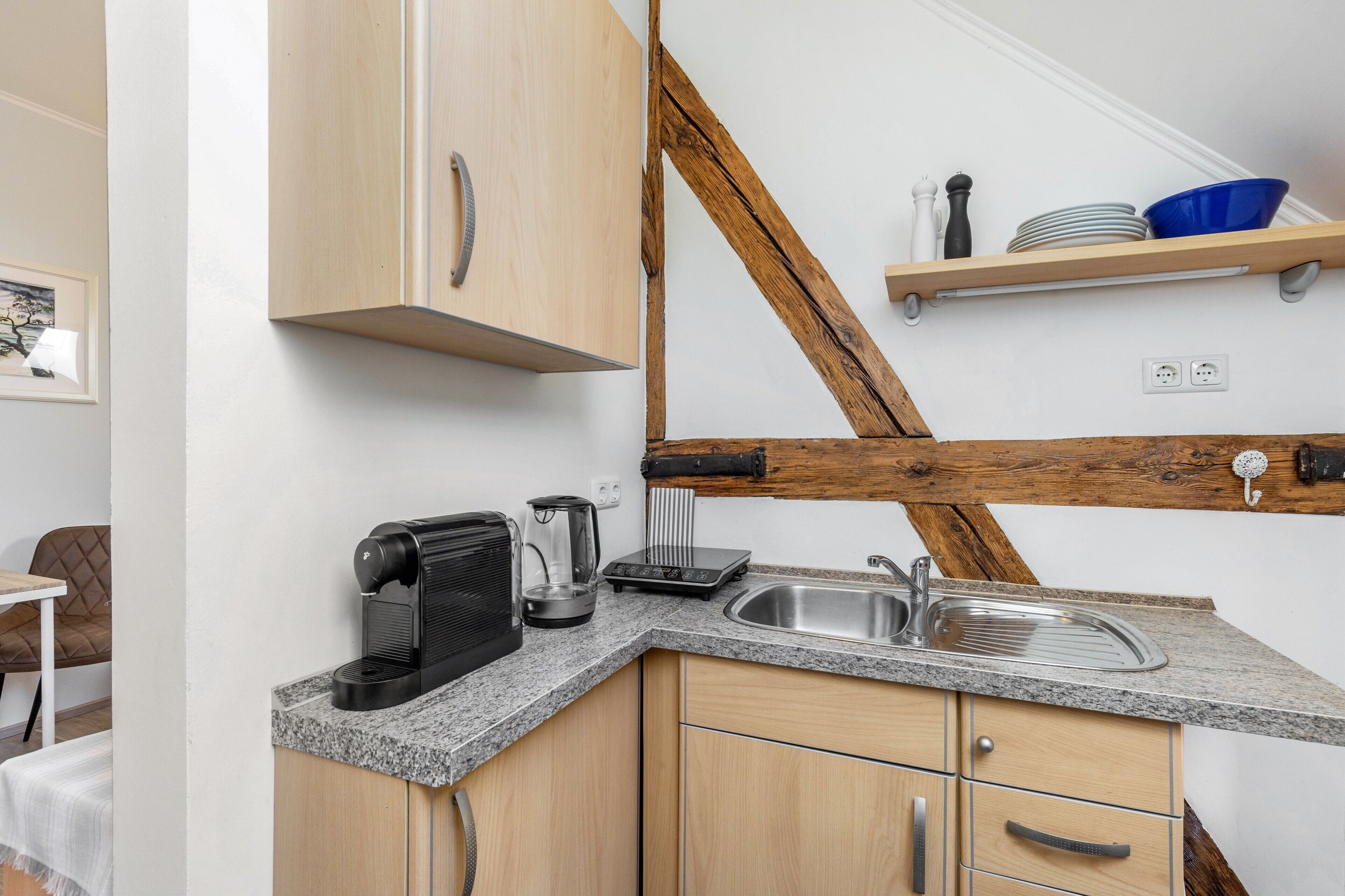 A kitchen with a granite countertop, a coffee maker, a toaster, a sink, and wooden beams.