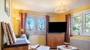 A room with a wooden cabinet, a television, a table with a vase, and a window with curtains. - Apartment 'Blackforest' with Shared Terrace, Shared Garden and Wi-Fi (Sankt Georgen)