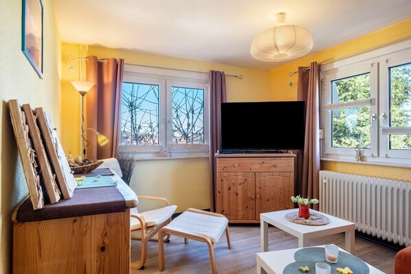 A room with a wooden cabinet, a television, a table with a vase, and a window with curtains.