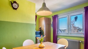 A dining area with a wooden table, white chairs, a vase with flowers, a wall clock, and a window with curtains. - Apartment 'Blackforest' with Shared Terrace, Shared Garden and Wi-Fi (Sankt Georgen)