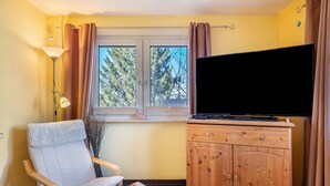 A room with a TV, a chair, a wooden cabinet, and a window with curtains. - Apartment 'Blackforest' with Shared Terrace, Shared Garden and Wi-Fi (Sankt Georgen)