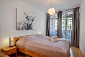 Une chambre à coucher comprenant un lit, une table de chevet, une lampe fixée au mur, un luminaire décoratif, une fenêtre avec des rideaux et un tableau représentant un taureau accroché au mur.