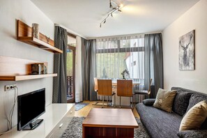 Un salon moderne doté d’un téléviseur à écran plat, d’étagères en bois, d’un canapé, d’une table basse et d’un coin repas avec des chaises.