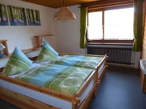 A wooden bed with green floral bedding, a hanging lamp, and a window with curtains. - Holiday Home 'Am Bach' with Mountain View, Private Terrace and Wi-Fi (Wieden)