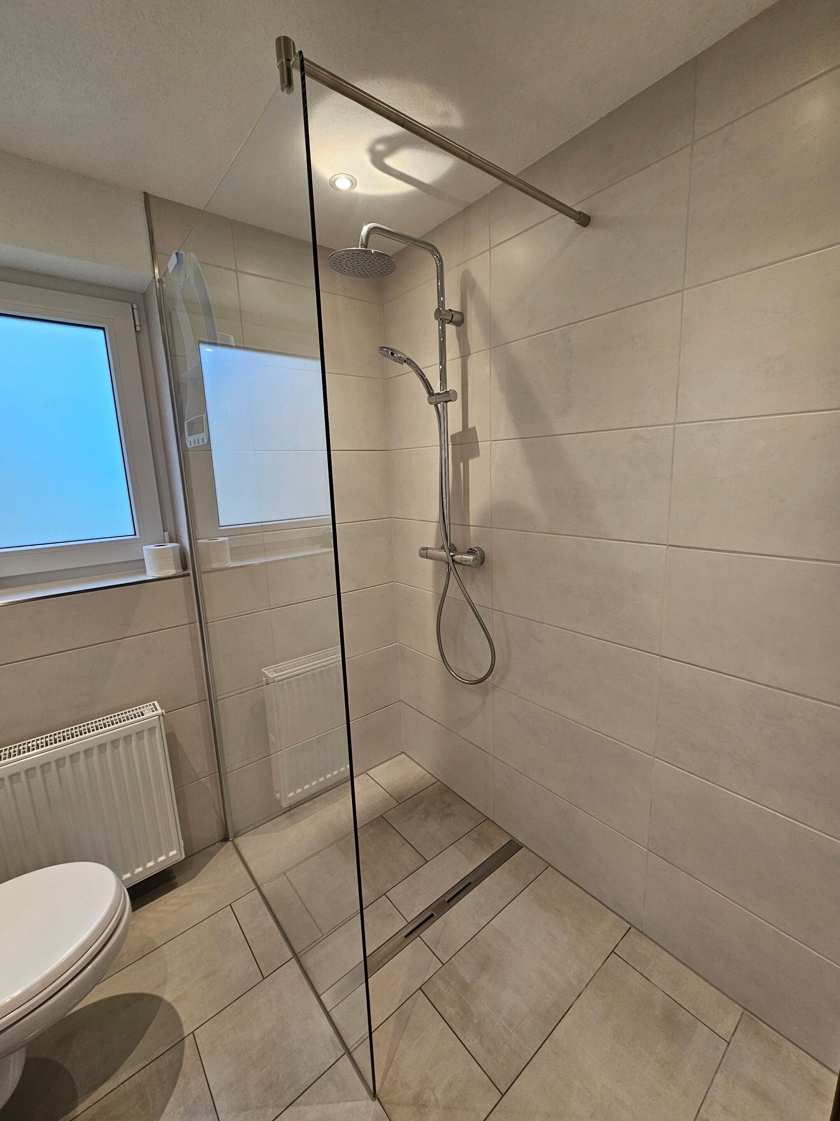 Ein Badezimmer mit Duschkabine aus Glas, Toilette und Fenster.