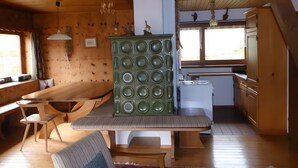 A wooden interior with a dining table, chairs, a bench, a green cabinet, a white refrigerator, and a window.