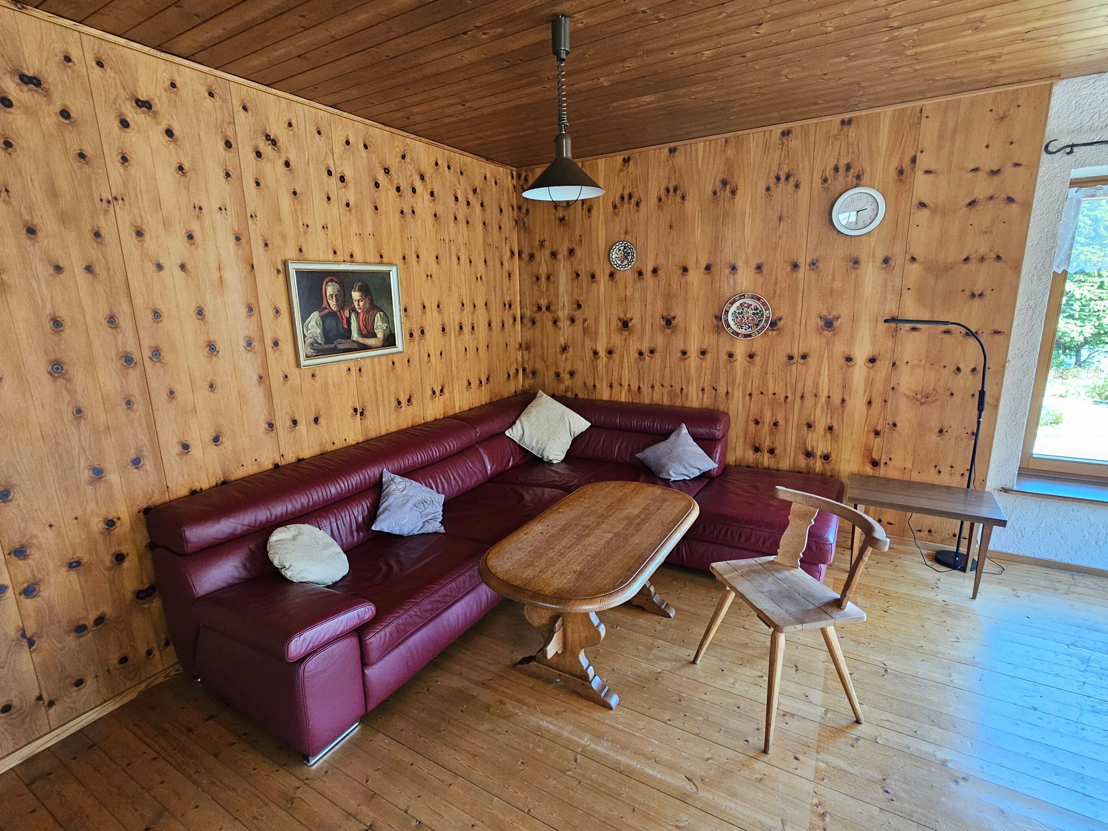 Una stanza con pannelli in legno, un divano in pelle rossa, un tavolino in legno e una piccola sedia di legno.
