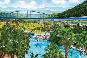 Una grande piscina all'aperto con palme, un ponte di vetro e vista su un paesaggio montuoso.