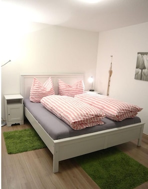 Een slaapkamer met een bed, nachtkastje, lamp en een groen vloerkleed.