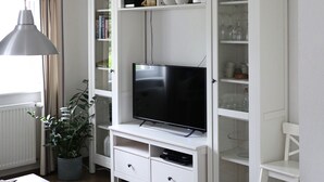 A living room with a TV, white cabinets, a potted plant, and a striped chair. - Apartment 'Am Brunnen' with Shared Terrace, Shared Garden and Wi-Fi (Titisee-Neustadt)