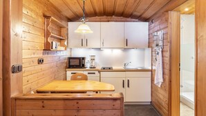 A compact kitchen with wooden walls, a wooden table, cabinets, a microwave, and a hanging light fixture. - Apartment 'Museumsblick' with Mountain View and Wi-Fi (Mittenwald)
