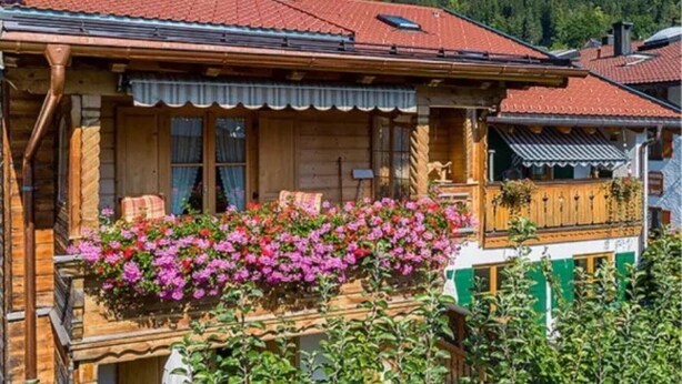 A traditional wooden house with a balcony, a red tiled roof, and a forested background. - Apartment 'Museumsblick' with Mountain View and Wi-Fi (Mittenwald)
