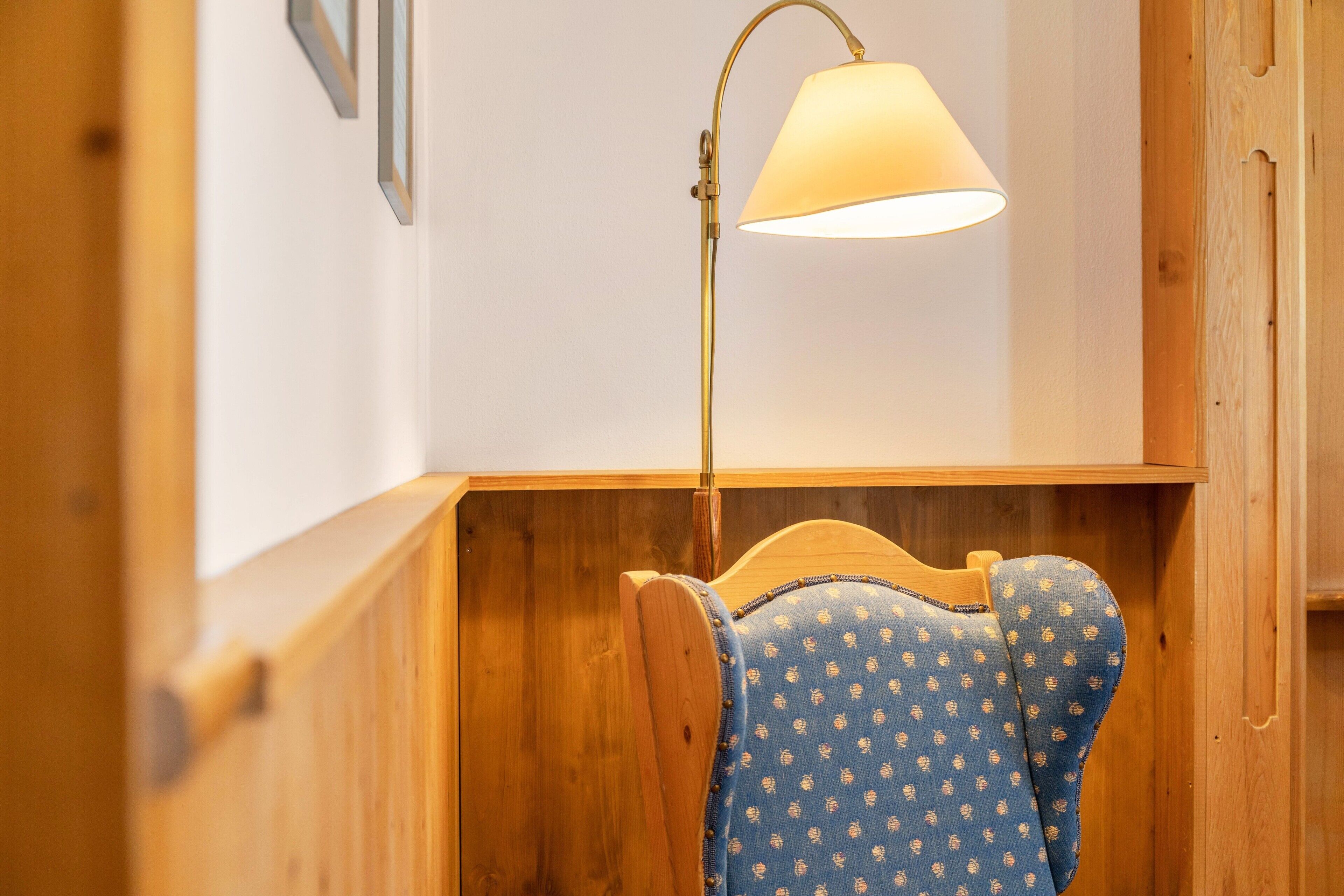 Een houten bank met een blauw gestreept kussen, een vloerlamp en een houten wand.