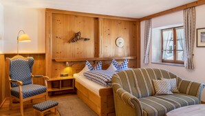 A wooden cabin interior with a bed, a striped sofa, a blue armchair, and a small table. - Apartment 'Museumsblick' with Mountain View and Wi-Fi (Mittenwald)