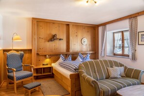 Interior de una cabaña de madera con una cama, un sofá a rayas, un sillón azul y una mesita.