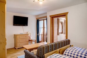 A room with a television mounted on the wall, a wooden dresser, a dining table, a sofa with patterned cushions, and a window with curtains. - Apartment 'Karwendelblick' with Mountain View, Balcony and Wi-Fi (Mittenwald)
