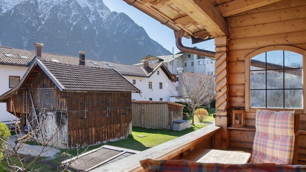Eine Holzhütte mit Blick auf schneebedeckte Berge, einer hölzernen Bank und einem Fenster mit Ausblick auf die umliegenden Gebäude.