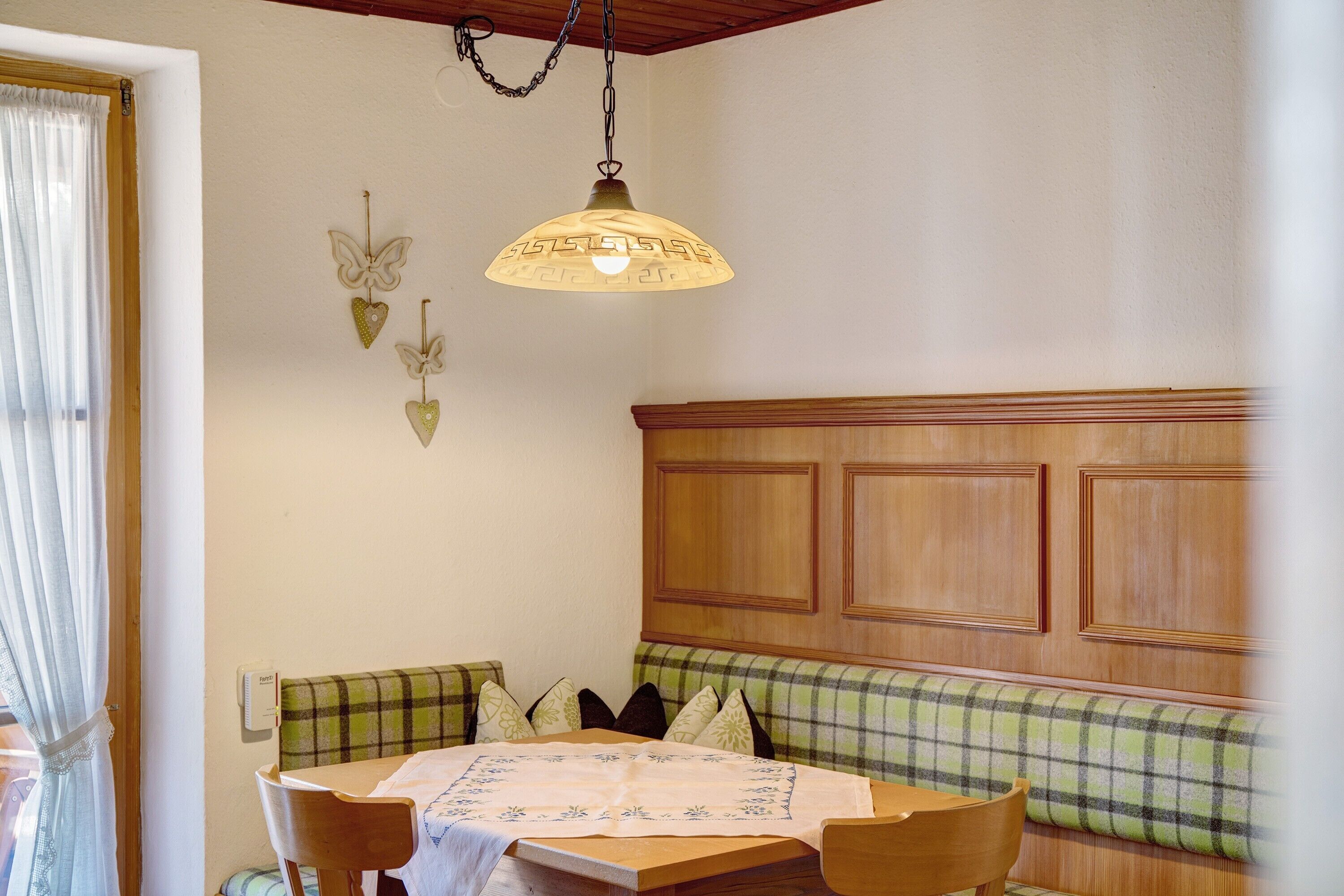 A dining area with a table, chairs, a bench, a hanging light fixture, and a wall-mounted thermostat.