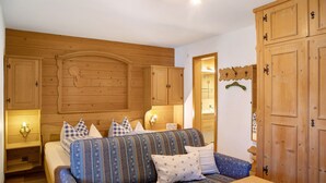 Ein gemütliches Zimmer mit Holzboden, einer Couch mit gemusterten Kissen, einem Holztisch und Holzschränken.