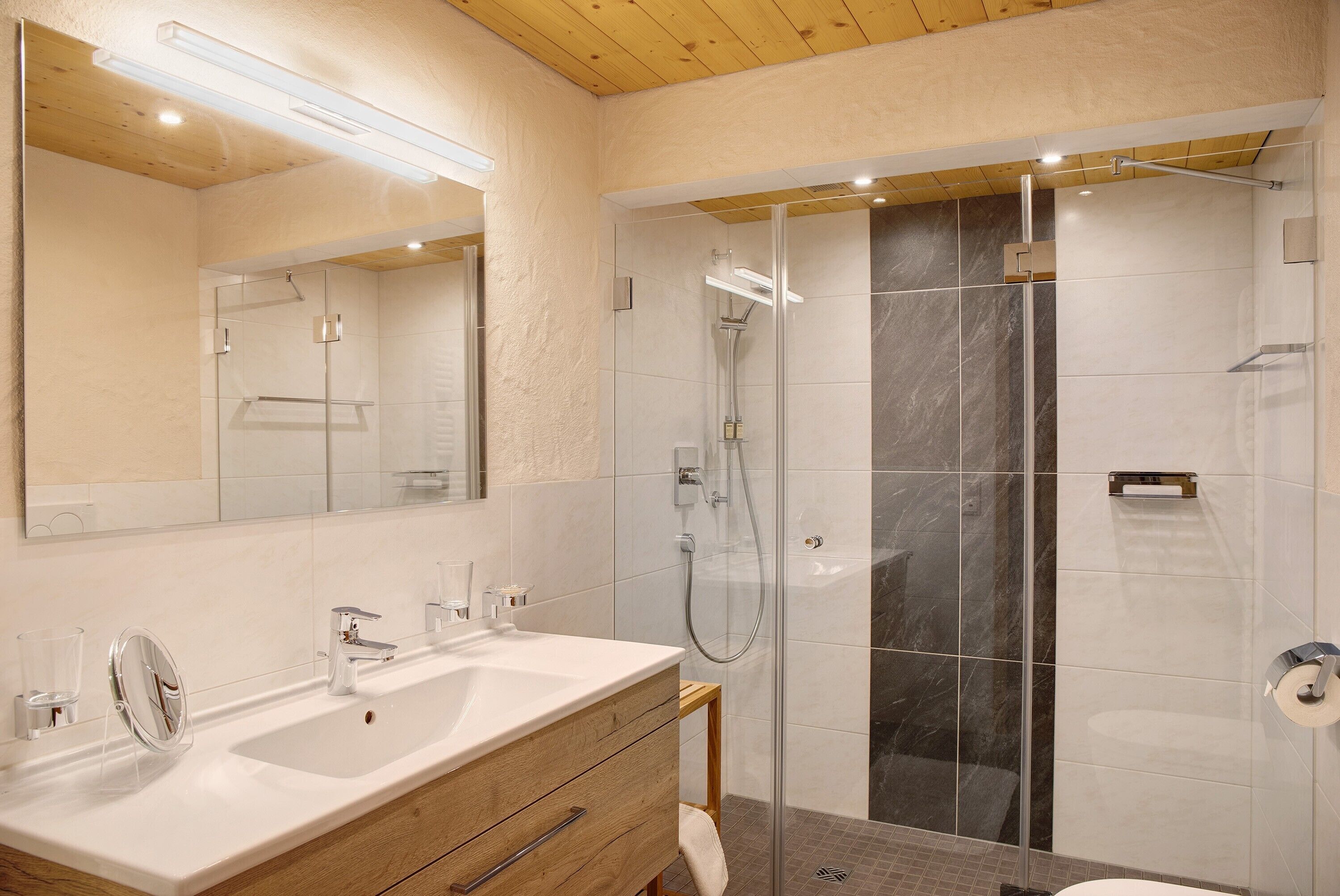 Ein modernes Badezimmer mit einem großen Spiegel, zwei Waschbecken, einer Dusche und einem Holzbadezimmer.