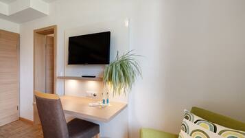 Una habitación moderna con un escritorio de madera, un televisor montado encima, una silla, una mesita pequeña y un sofá verde.