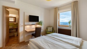 A hotel room with a bed, a desk with a TV, a chair, a window with a view, and a plant. - Room 'Panorama' with Shared Terrace, Shared Garden and Wi-Fi (Dornstetten)