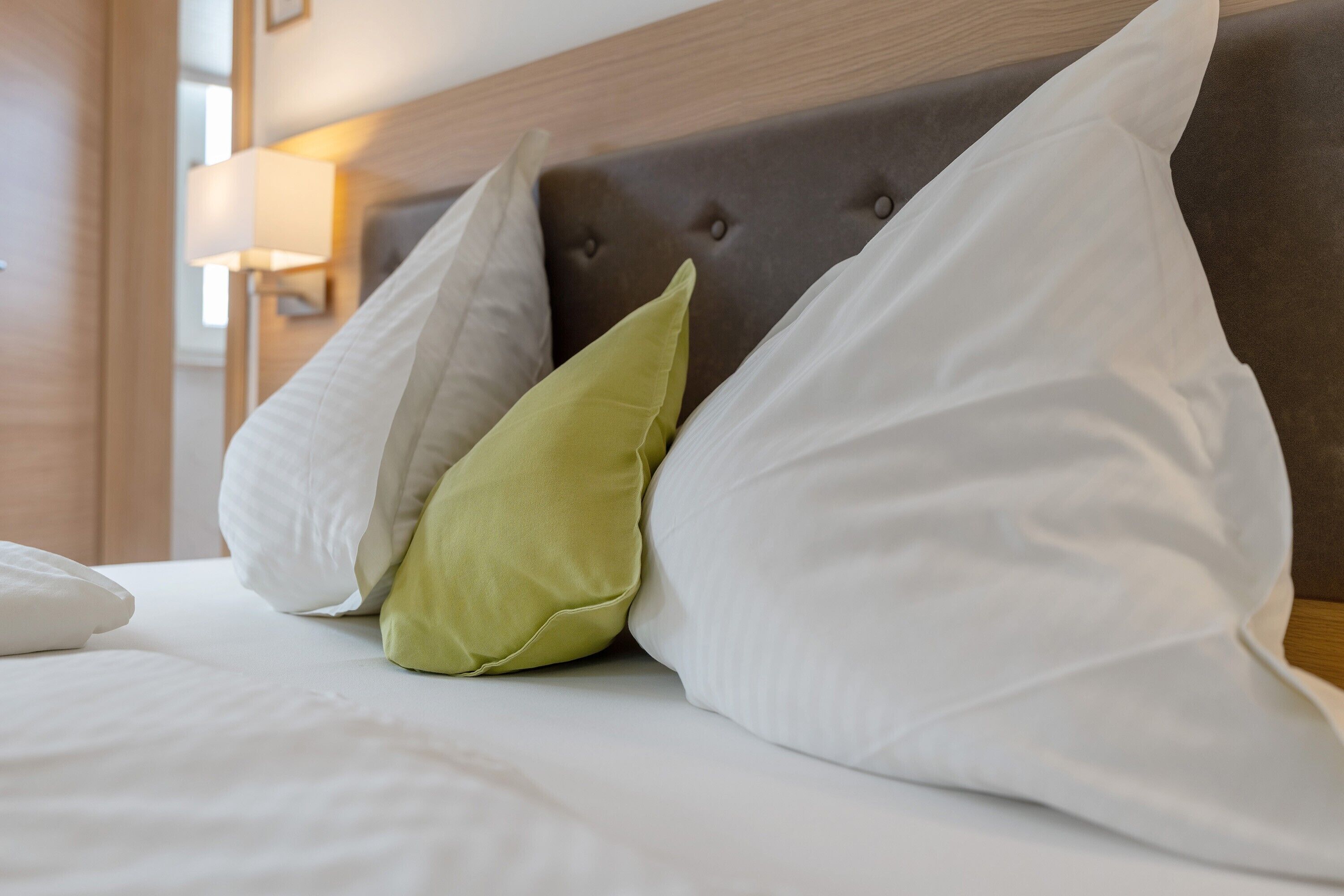 Een bed met hoofdbord, kussens en een bedlampje.