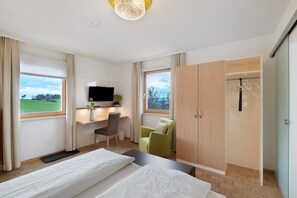 A hotel room with a bed, desk, chair, wardrobe, and a TV.