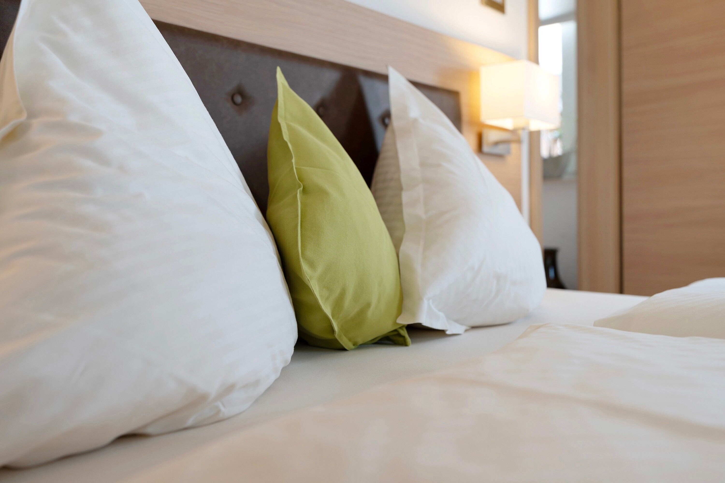 A bed with white bedding and a green pillow.
