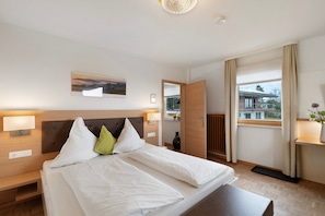 A hotel room with a large bed, bedside tables, a nightstand, a window with curtains, and a view of the outside.