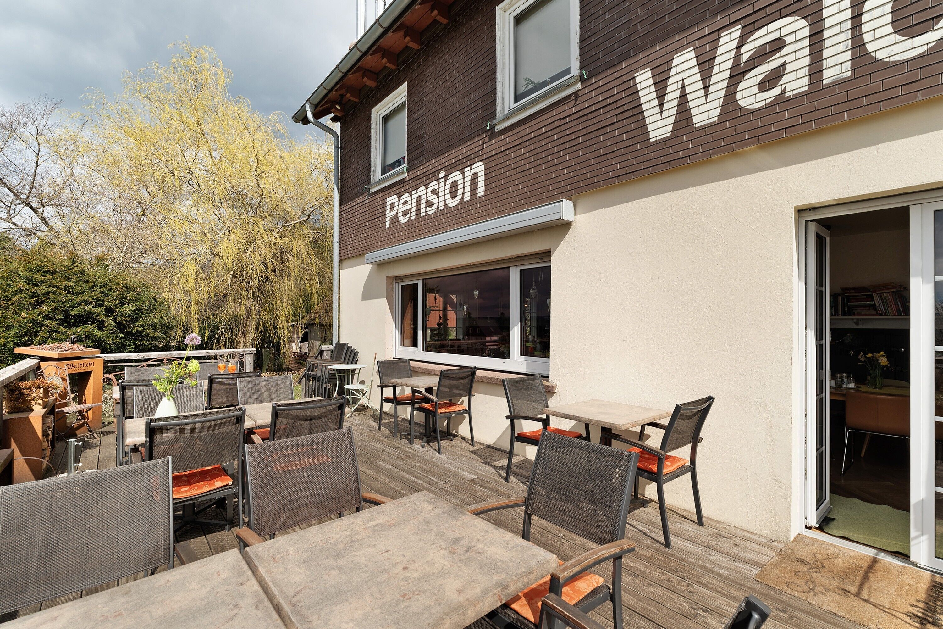 A patio area with outdoor seating and a building with a 'Pension' sign.