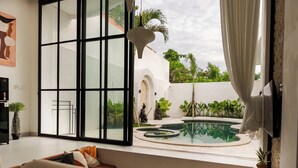 A modern living room with a large glass door leading to a pool area, featuring a minimalist design with a sofa and decorative pillows. - Tropical 2BR Private Villa, 6min Pererenan Beach (Munggu)