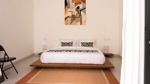 A bedroom with a bed, a chair, a wall-mounted artwork, and bedside tables. - Tropical 2BR Private Villa, 6min Pererenan Beach (Munggu)