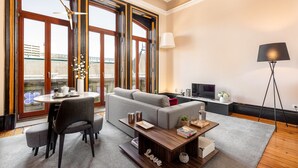 A modern living room with a sofa, a dining table, and a TV. Large windows provide natural light and a view of the city. - Cosy apartment in heart of Porto (Oporto)