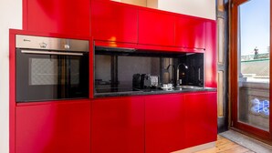 A modern kitchen with red cabinetry, a built-in oven, and a coffee machine. - Cosy apartment in heart of Porto (Oporto)