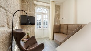 Una sala de estar moderna con una pared de piedra, un televisor de pantalla plana montado en la pared, un sillón de cuero marrón, un sofá beige y una puerta blanca con ventanal.