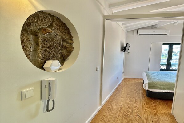 A modern hotel room with a stone wall feature, a phone, an air conditioning unit, and a bed with a view.