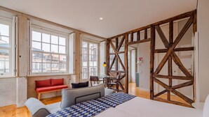 A bedroom with a large bed, a bench, a table, and a view of the city through large windows. - Pretty apartment with modern comforts (Oporto)
