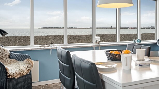 A dining area with a view of the sea, a white table, black chairs, and a hanging light fixture. - "Nyalle" - 50m to the fjord by Interhome (Struer)