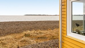 A coastal view from a yellow building with a window overlooking a pebbled beach and calm sea. - "Nyalle" - 50m to the fjord by Interhome (Struer)