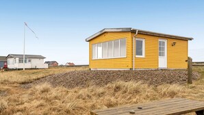 A yellow building with a white door and windows, surrounded by dry grass and a wooden picnic table. - "Nyalle" - 50m to the fjord by Interhome (Struer)