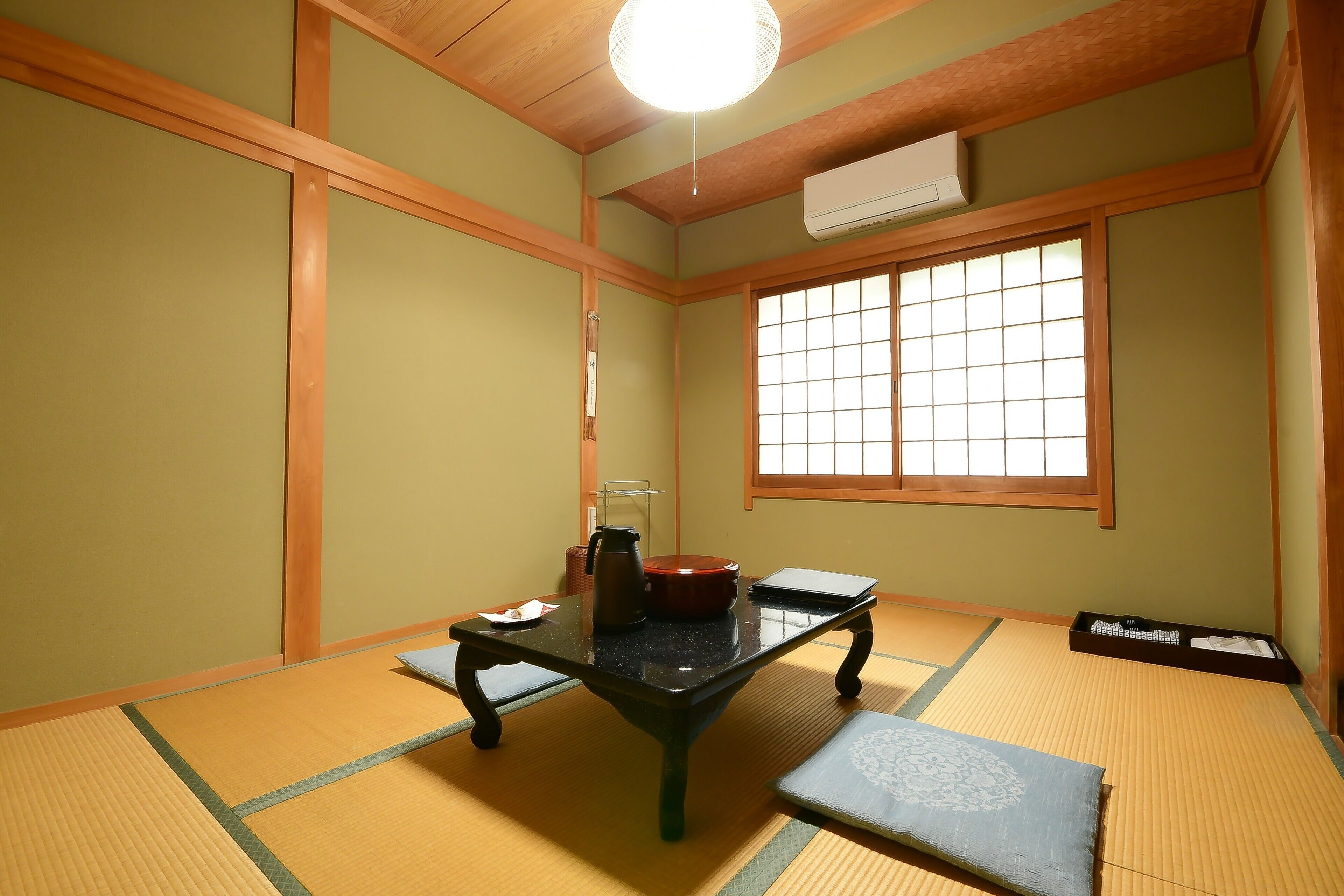 Een traditionele Japanse kamer met tatami vloerbedekking, een lage tafel met waterkoker, een rode pot en een zwarte dienblad met spullen.