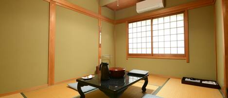 Een traditionele Japanse kamer met tatami vloerbedekking, een lage tafel met waterkoker, een rode pot en een zwarte dienblad met spullen.