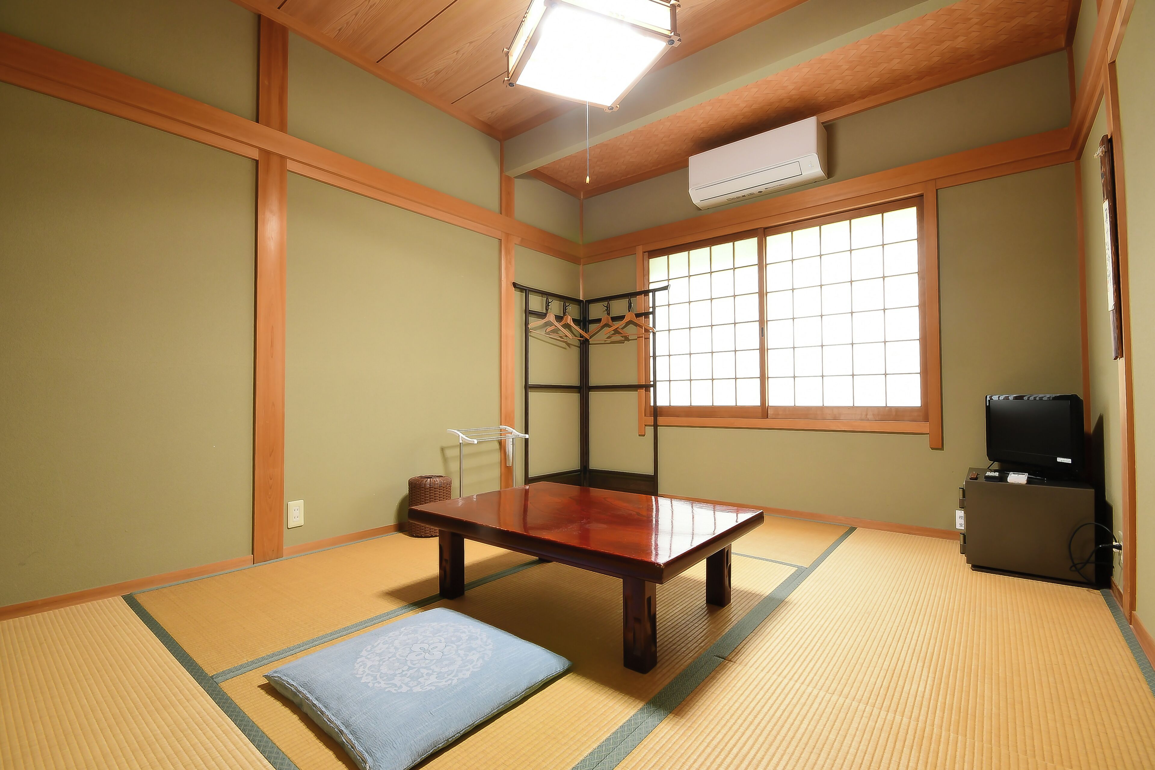 A traditional Japanese room with tatami flooring, a low wooden table, a television, and a sliding door.